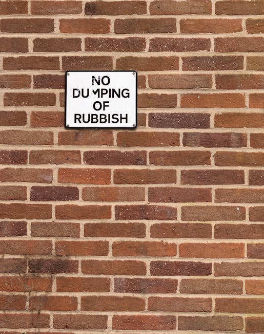 A rectangular black and white sign mounted on a red brick wall reads 'NO DUMPING OF RUBBISH' in bold black letters. The wall features horizontal rows of reddish-brown bricks with light gray mortar, an